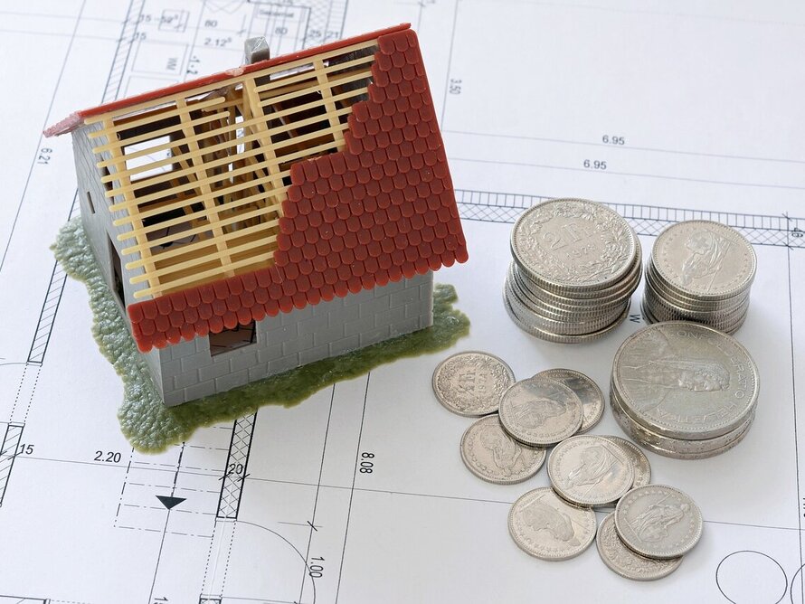 Hausmodell, Bauplan und Münzen als Symbol für Wohnungsbau und Baugenehmigungen