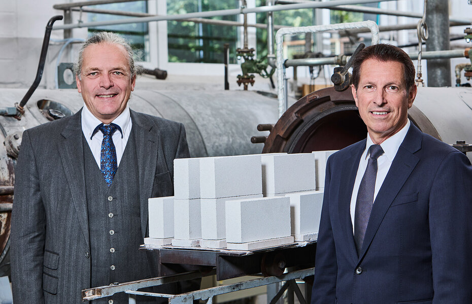 Frederic Dörlitz, Vorstandsvorsitzender, und Roland Meißner, Geschäftsführer des Bundesverbandes Kalksandsteinindustrie e. V. vor Produktionsanlagen und Kalksandsteinen.